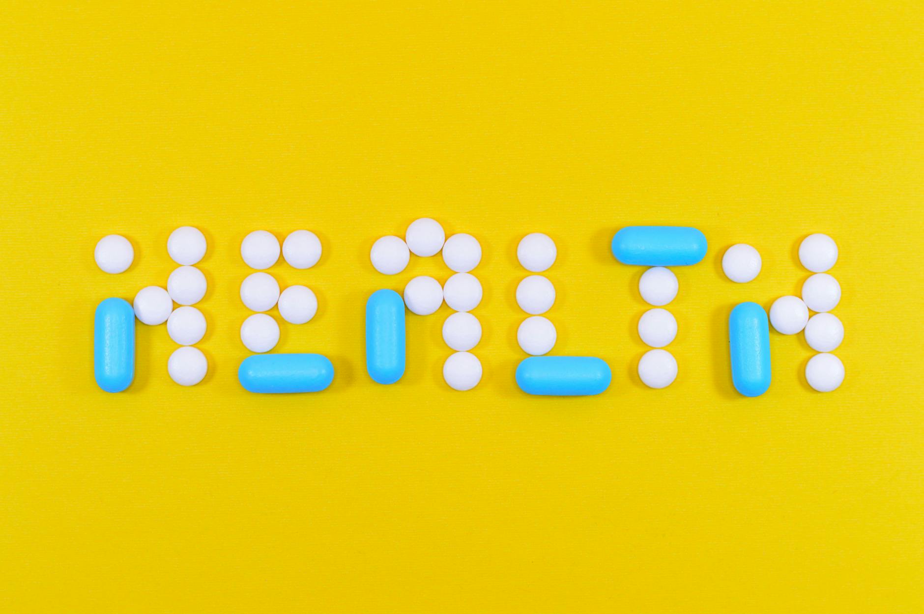 white and blue health pill and tablet letter cutout on yellow surface